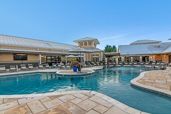 A large outdoor swimming pool surrounded by a stone patio and lounge chairs